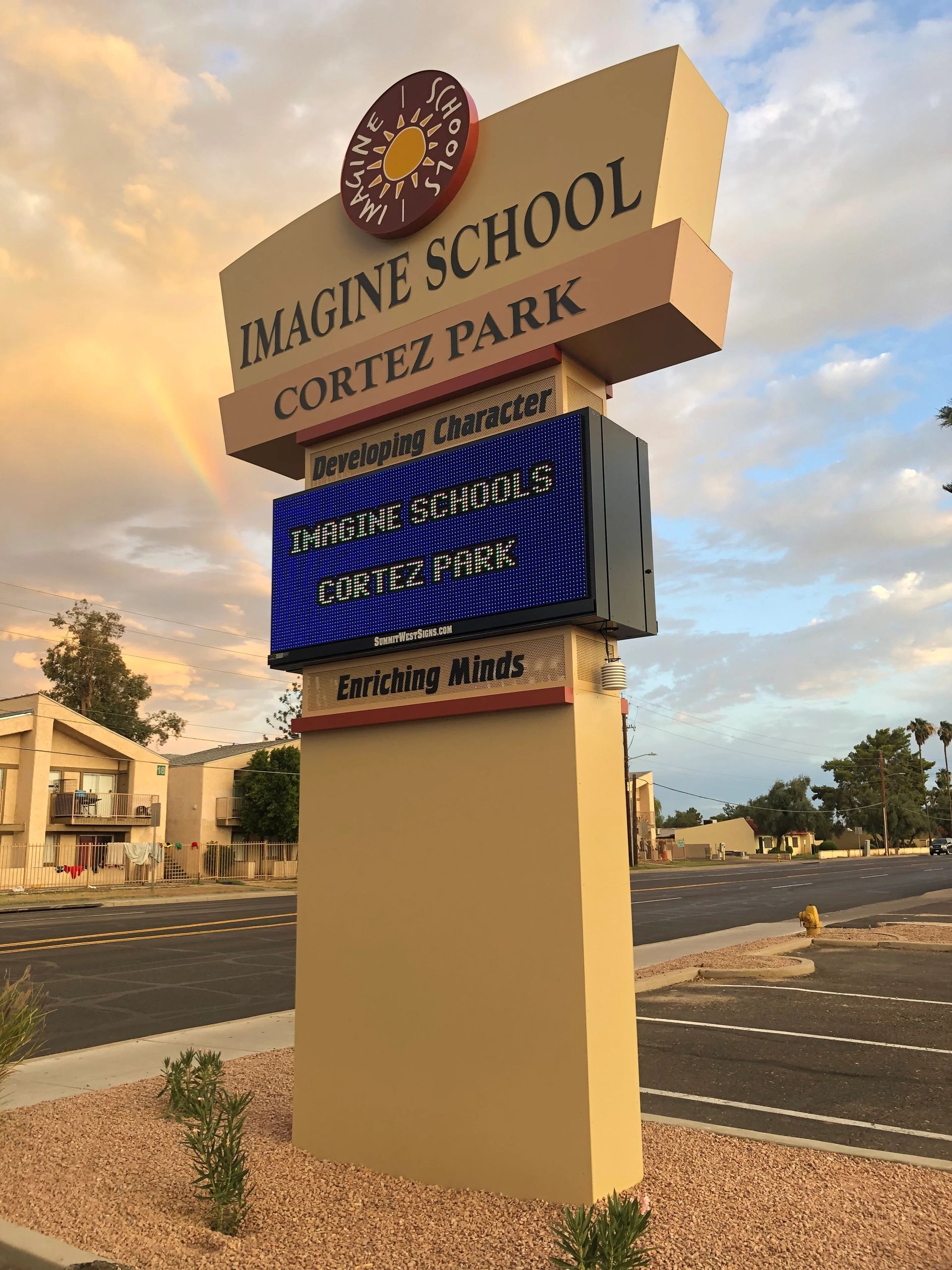A large sign for imagine school cortez park is sitting on the side of the road.