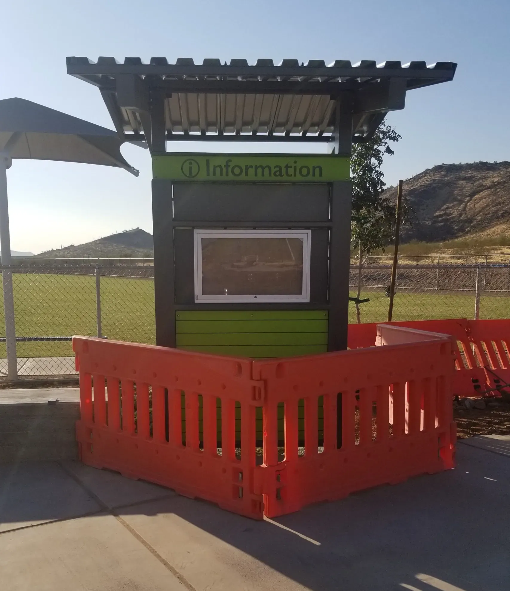 A green information booth is surrounded by orange barriers