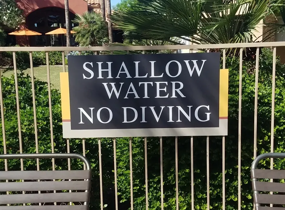 A sign on a fence says shallow water no diving