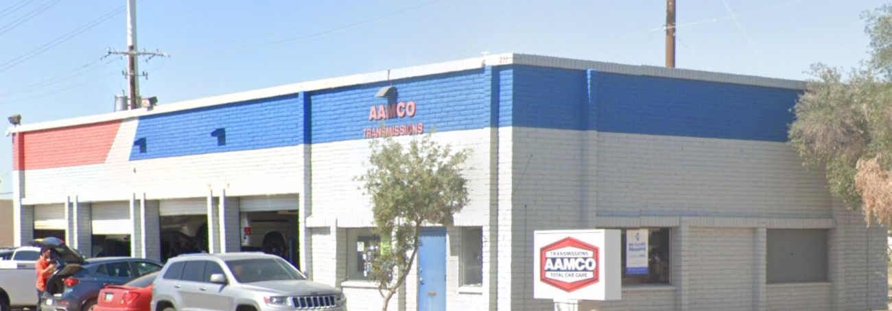 Single-story commercial building with blue and gray exterior, parked cars, and a sign near the entrance