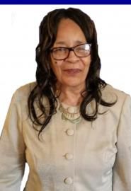 Portrait of a woman in glasses wearing a beige jacket and necklace against a white background