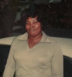 Person in a light green collared shirt standing beside a car at night, smiling at the camera.