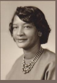 Black-and-white portrait of a woman wearing pearl necklace and earrings, facing slightly left and smiling softly
