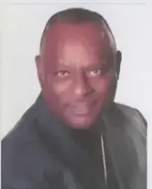 Portrait of a man in a dark jacket, facing the camera against a plain light background.