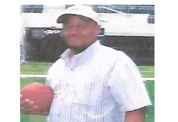 Person in a white shirt and cap holding a football on a field.