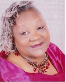 Smiling portrait of a woman in a magenta top and beaded necklace on a pale pink background