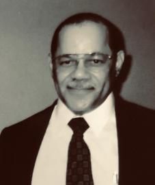 Black-and-white portrait of a smiling man in glasses, suit, tie, and white shirt.