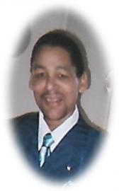 Formal portrait of a smiling person in a dark suit and striped tie, framed by a soft oval vignette.