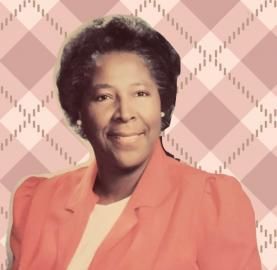 Smiling woman in a coral blazer against a pink plaid background