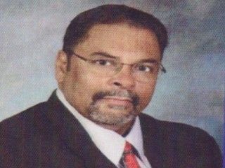 Formal portrait of a man in a dark suit, white shirt, and red tie, wearing glasses and a goatee.
