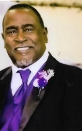 Smiling man in a black suit and purple tie with a purple boutonniere