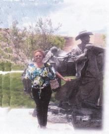 Woman posing beside a bronze statue in a garden with trees and a pond.