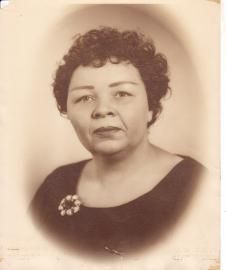 Sepia portrait of a woman with short curly hair wearing a dark dress and floral brooch, facing forward