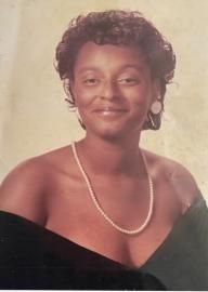 Studio portrait of a smiling person wearing a black dress and pearl necklace against a neutral background