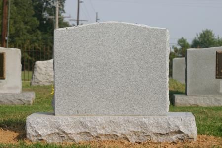 Blank gray granite gravestone in a cemetery, centered against other headstones and grass.