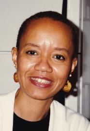Smiling person in a black top and white jacket against a light background