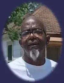 Man wearing glasses and a white shirt outdoors in front of a house, with a serious expression.