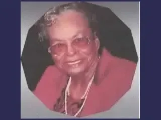 Portrait of a smiling person in glasses, wearing a red jacket and necklace against a dark background