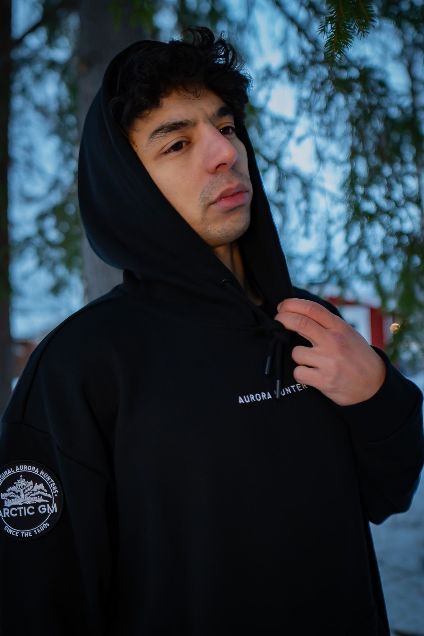 Male model wearing black Arctic GM hoodie in forest setting