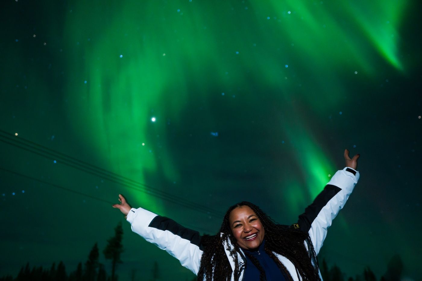 Guest standing under a vivid curtain of green Northern Lights during an Arctic GM tour in Lapland