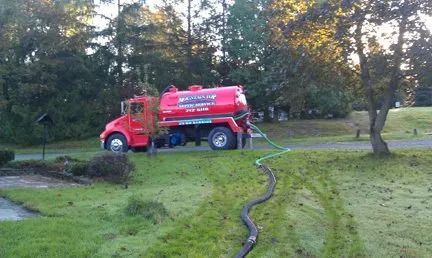 A red septic tank truck is parked in a grassy field.