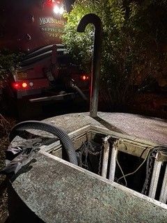 A hose is being used to pump water into a septic tank at night.