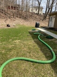 A green hose is laying on the grass in a yard.