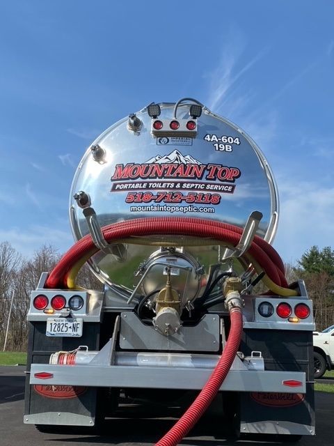 A tanker truck with a red hose attached to it is parked in a parking lot.