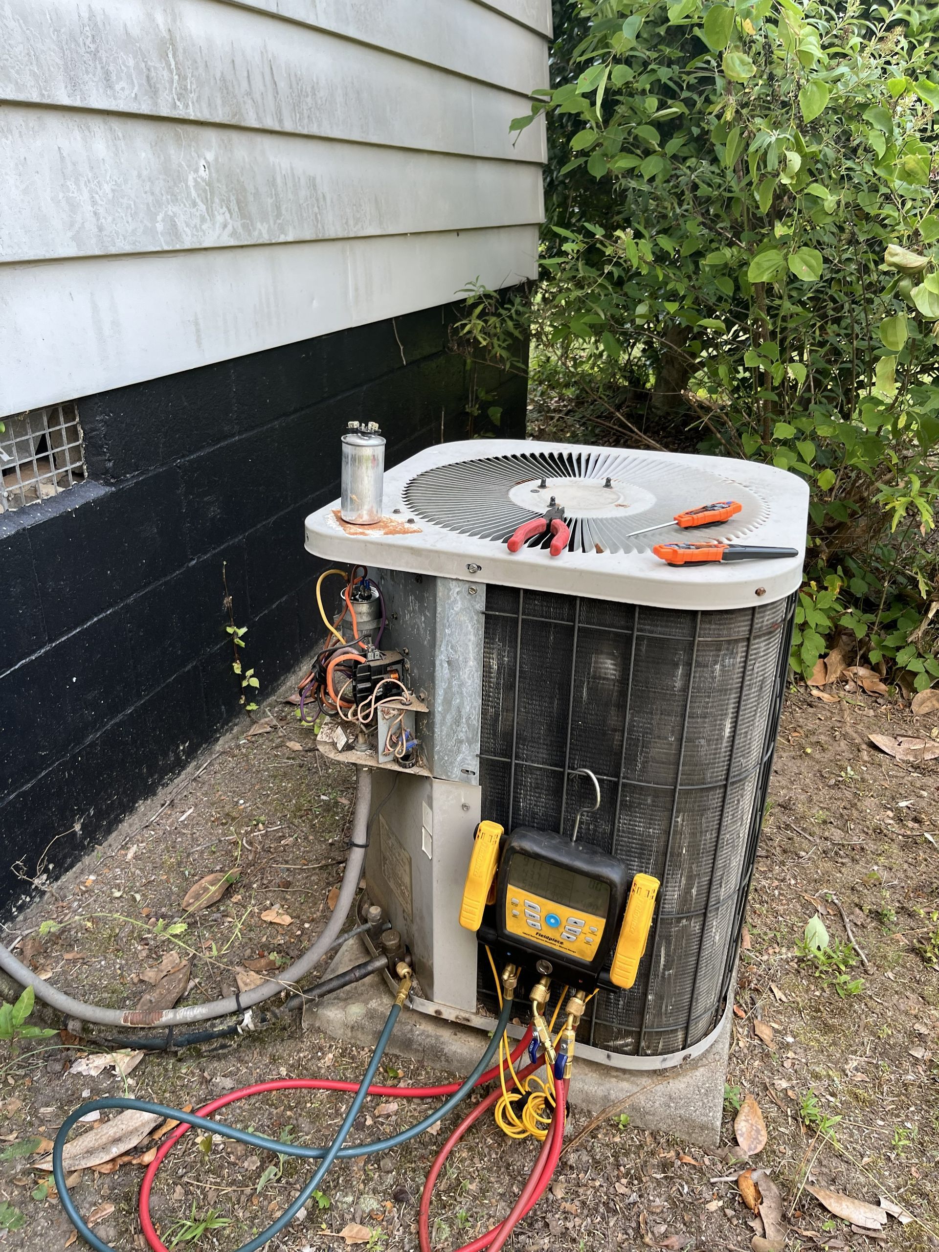 Outdoor electrical unit and cables beside a house, with tools on top and wires exposed.