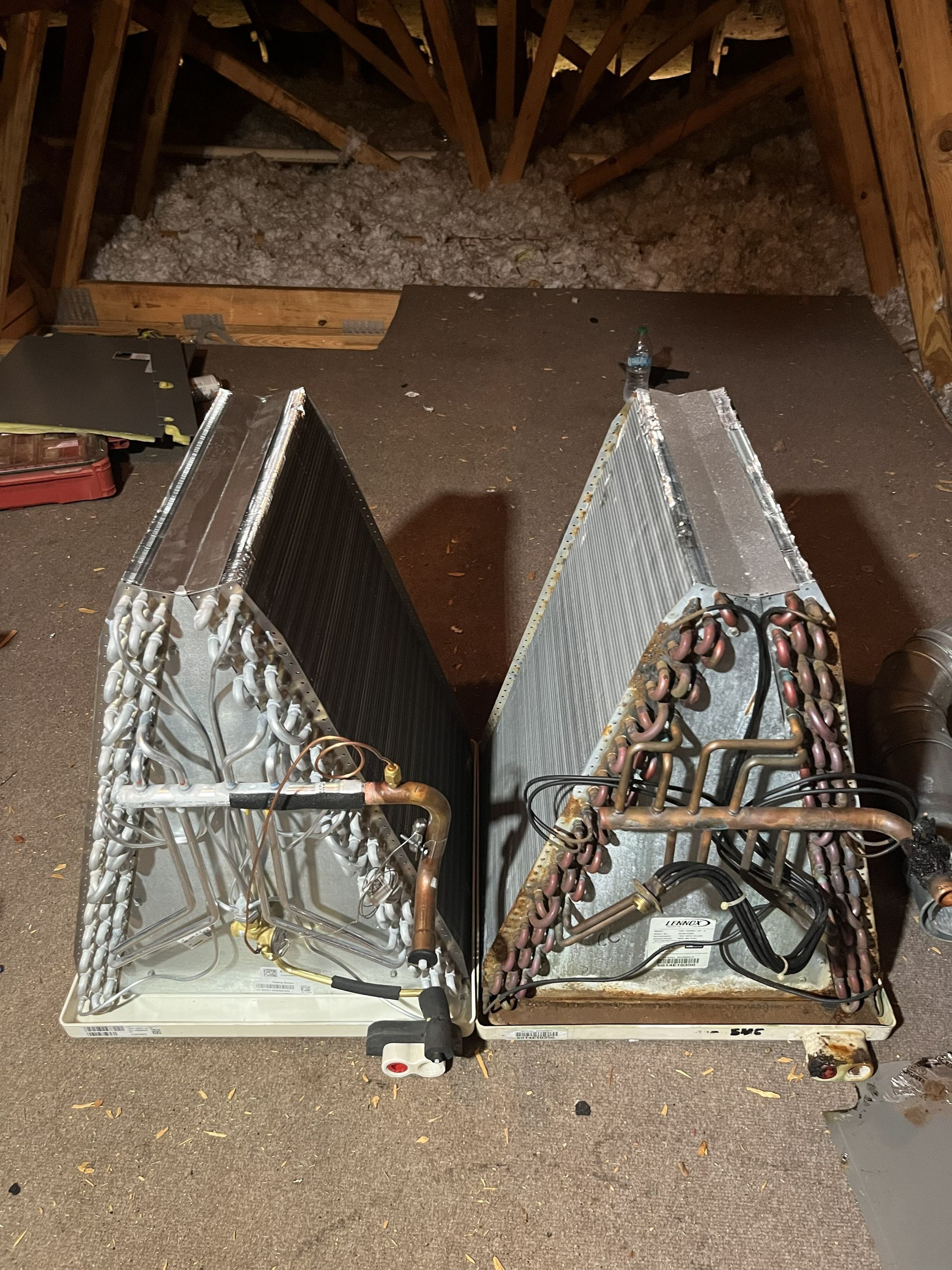 Two silver automotive radiators leaning side by side in an attic space, with exposed copper tubing.