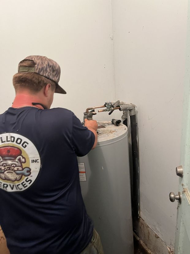Technician working on a water heater in a small utility room with white walls