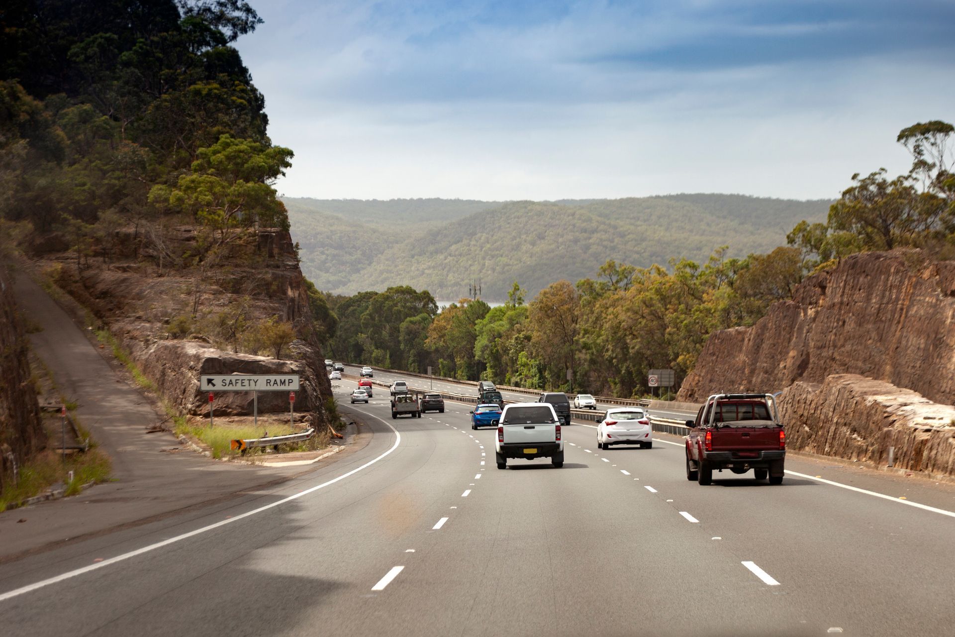 Cars are driving down a highway with mountains in the background.