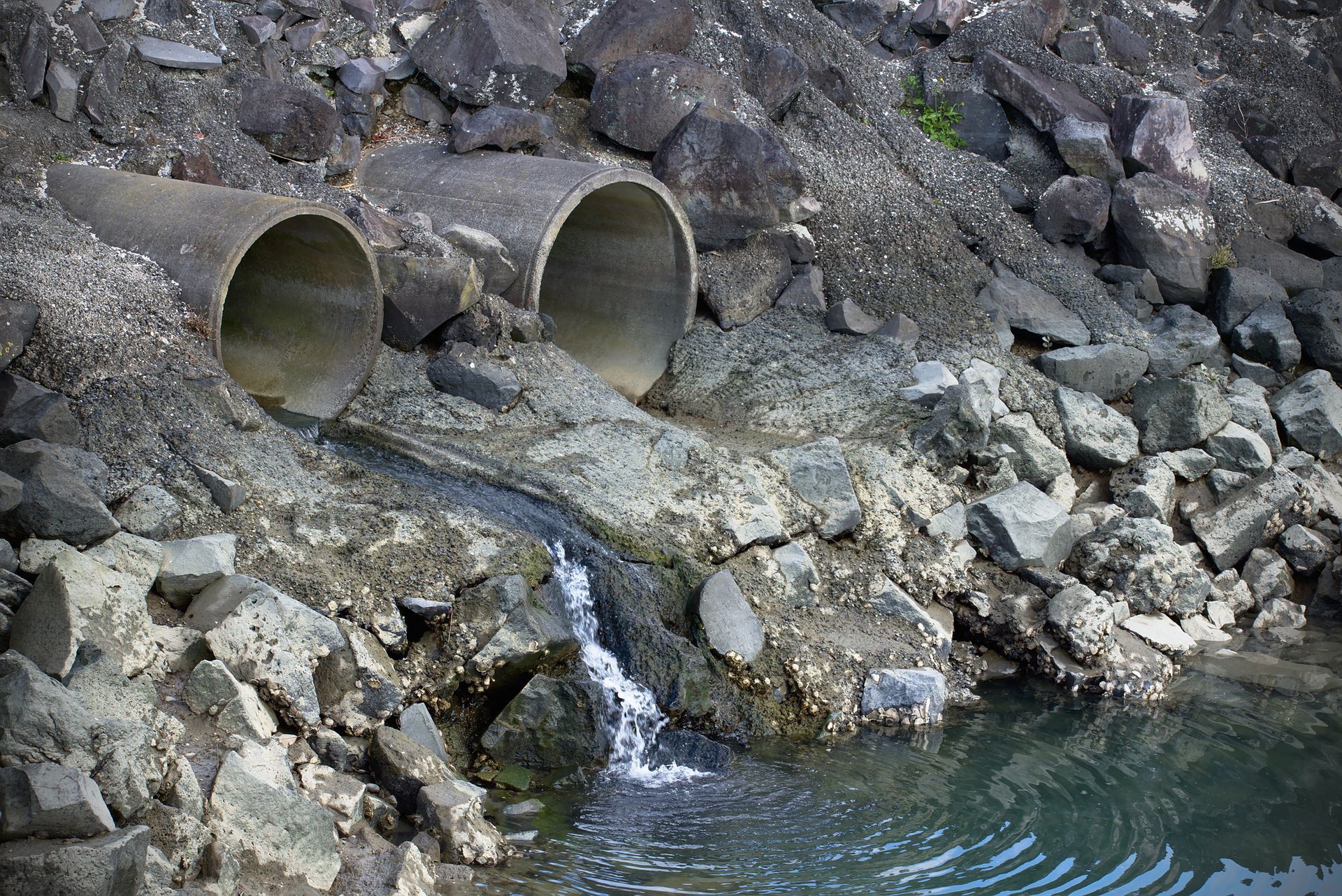A waterfall is coming out of a pipe in a rocky area.