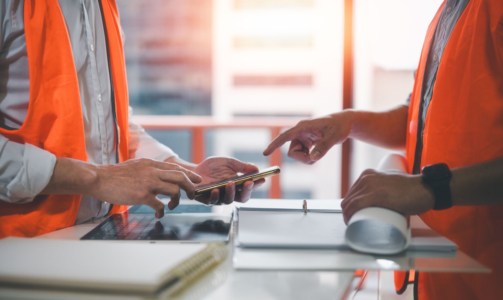 Two construction workers are looking at a tablet and a cell phone.