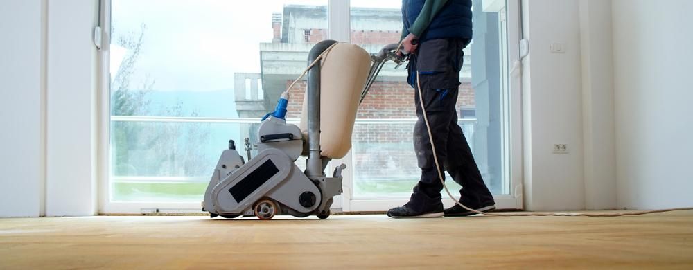 A Man Is Sanding A Wooden Floor With A Machine — Canberra Handyman Solutions In Wanniassa, ACT