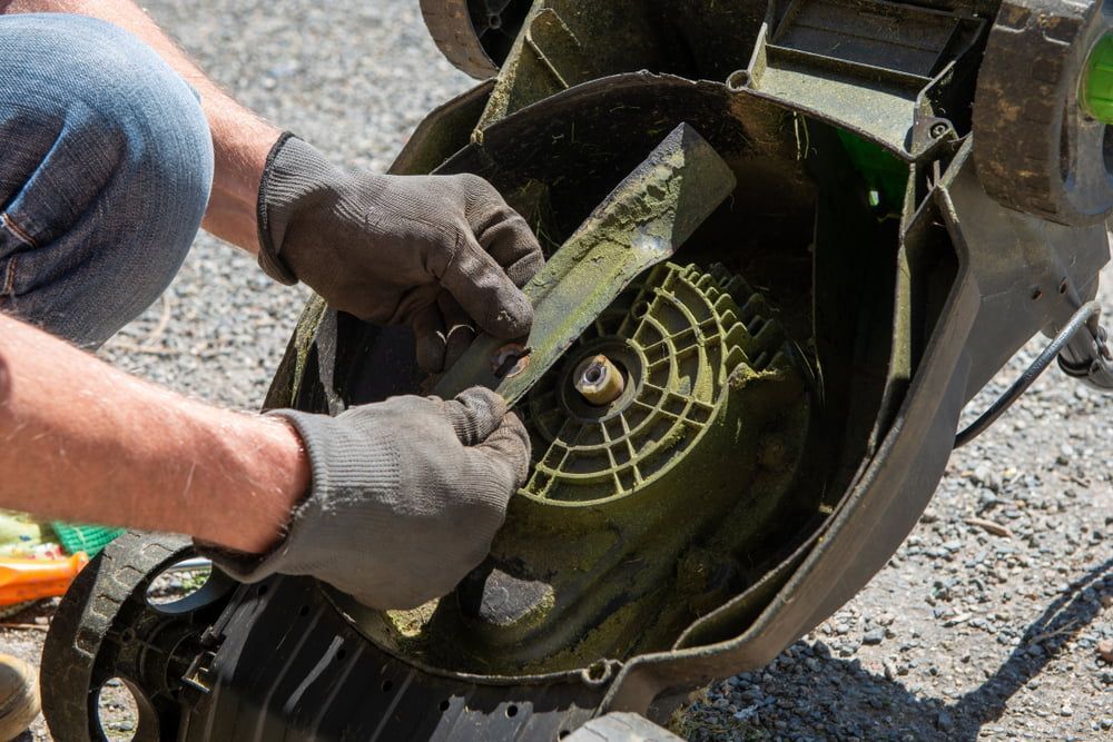 A Man Is Cleaning the Blade of A Lawn Mower — Stihl Shop Grafton in Iluka, NSW