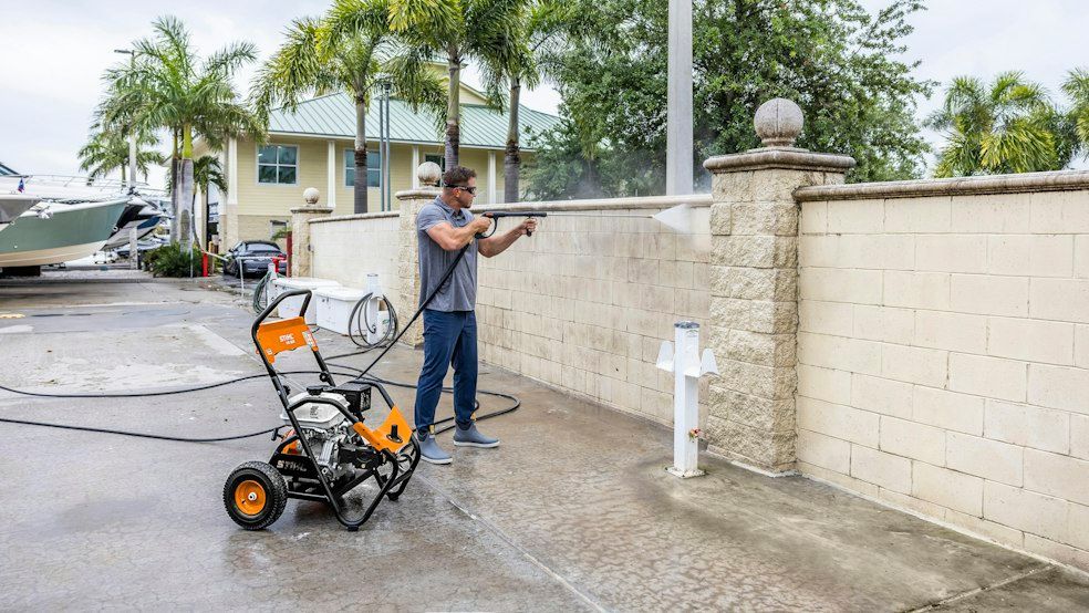 A Man Is Using a Pressure Washer to Clean a Sidewalk — Stihl Shop Grafton in Grafton, NSW