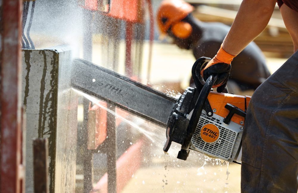 A Man Is Using a Chainsaw to Cut a Piece of Wood — Stihl Shop Grafton in Grafton, NSW
