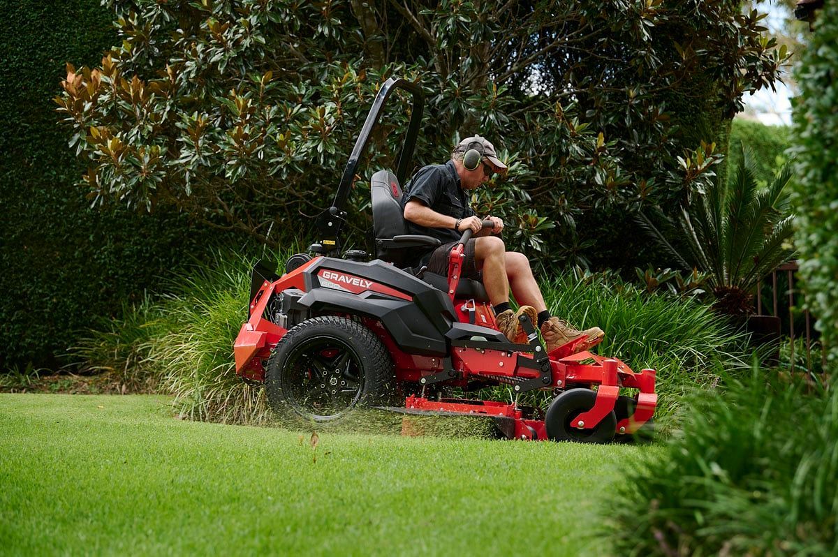 A Man Is Riding a Red Lawn Mower on A Lush Green Lawn — Stihl Shop Grafton in Yamba, NSW