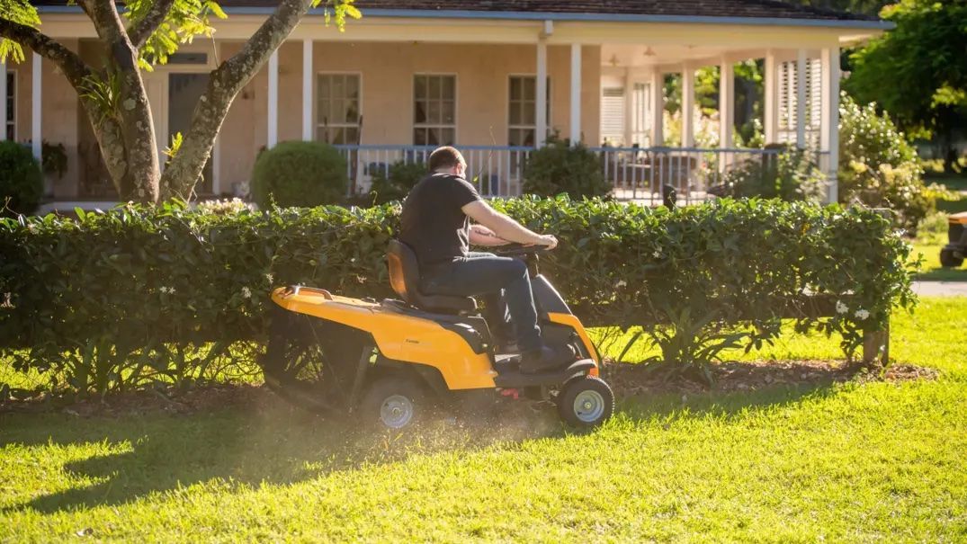 A Man Is Riding a Lawn Mower on A Lush Green Lawn in Front of A House — Stihl Shop Grafton in Grafton, NSW