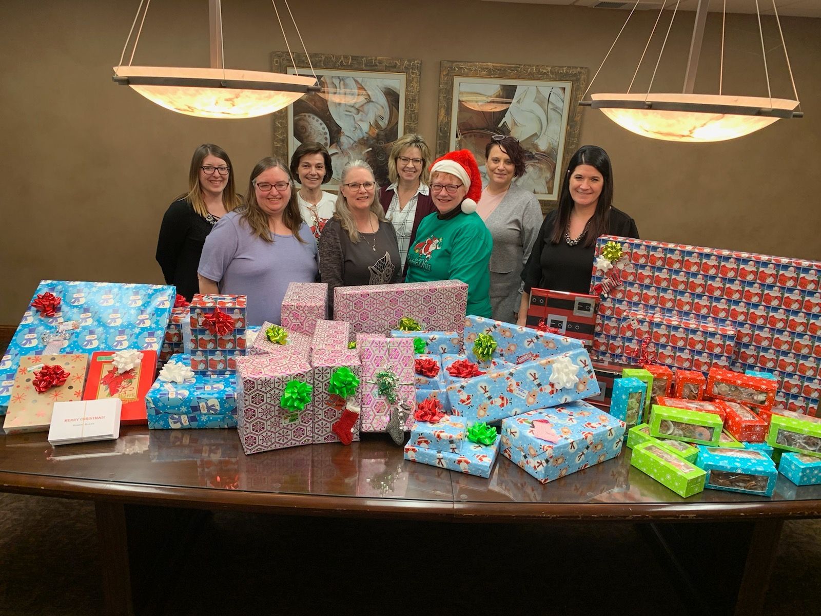 Group of people with wrapped gifts on a table, possibly for a holiday.