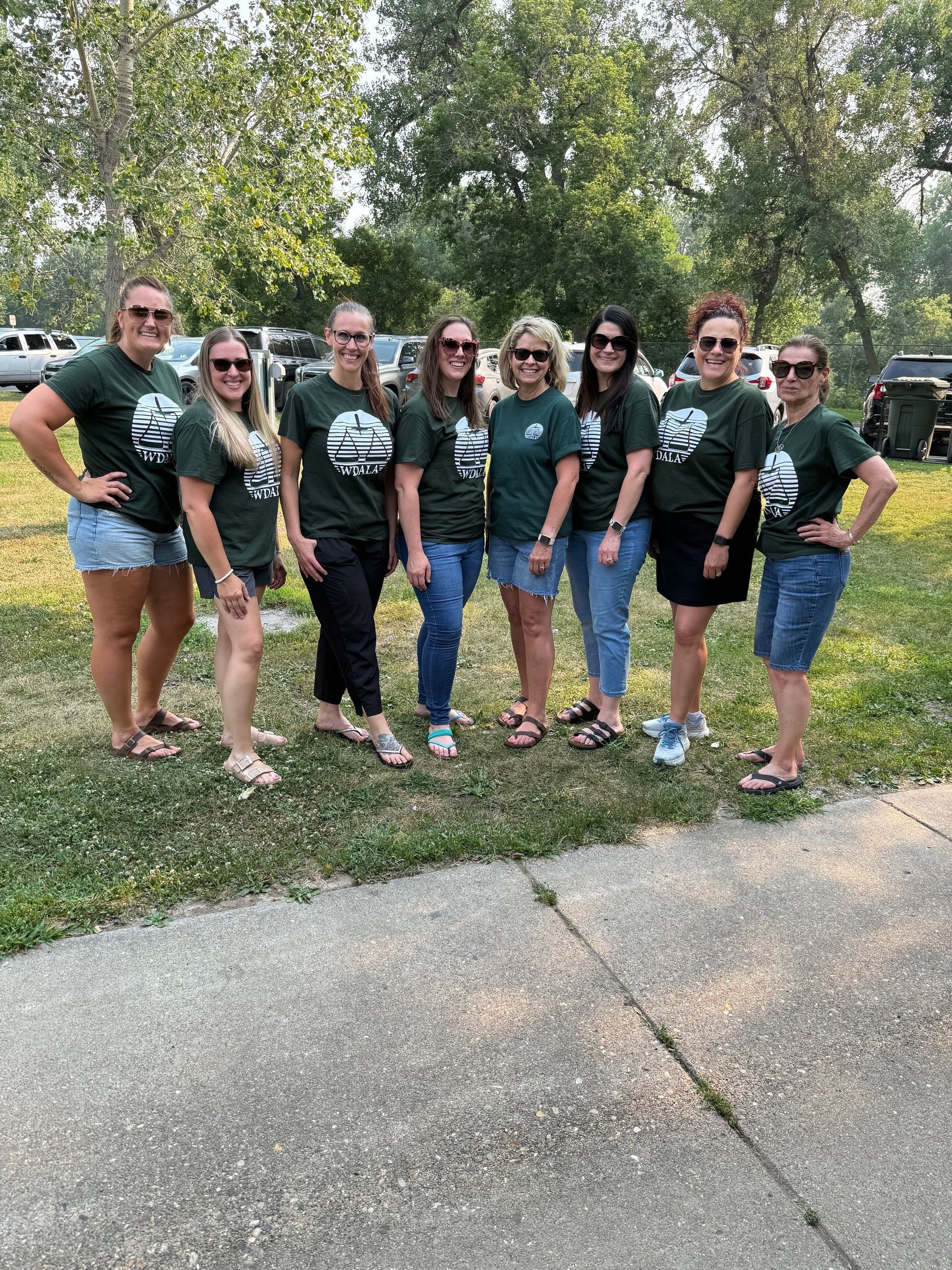 Group of eight women in matching green shirts, posing outdoors.