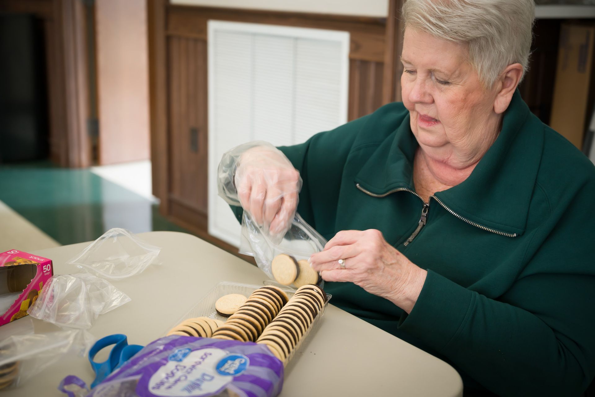 An elderly woman is sitting at a table with a bag of cookies.