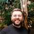 A man with a beard is smiling in front of a tree.
