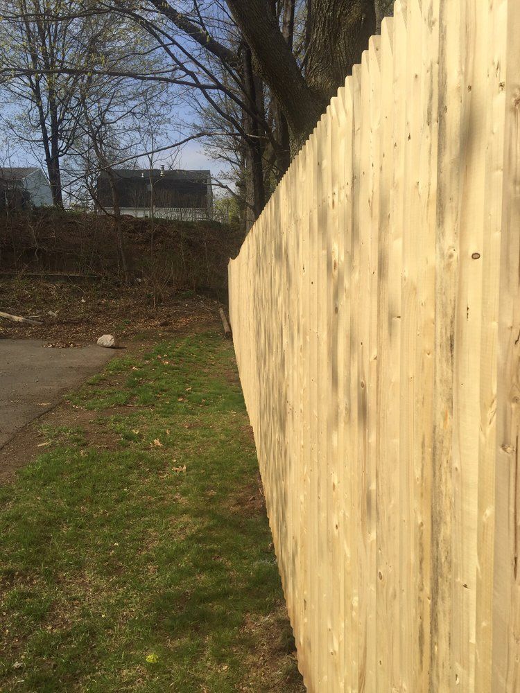 Wooden fence along a grassy area, curved perspective, with trees and a building in the background.