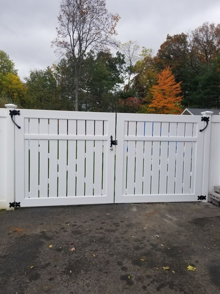 White double gate in front of a yard, trees in the background, asphalt surface.