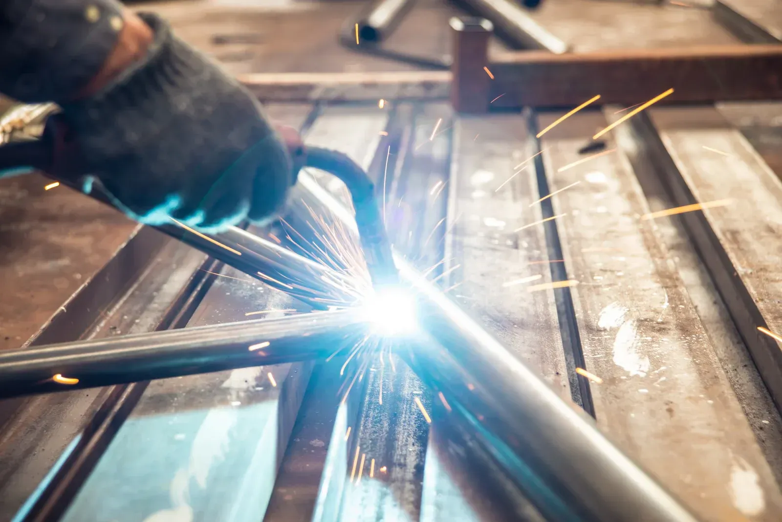 Welder in gloves welding metal tubes with bright sparks.
