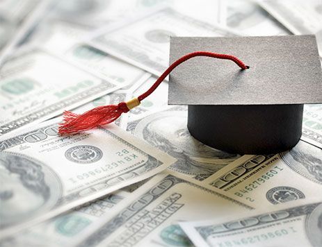 A graduation cap with a red tassel sitting on a pile of one hundred dollar bills.
