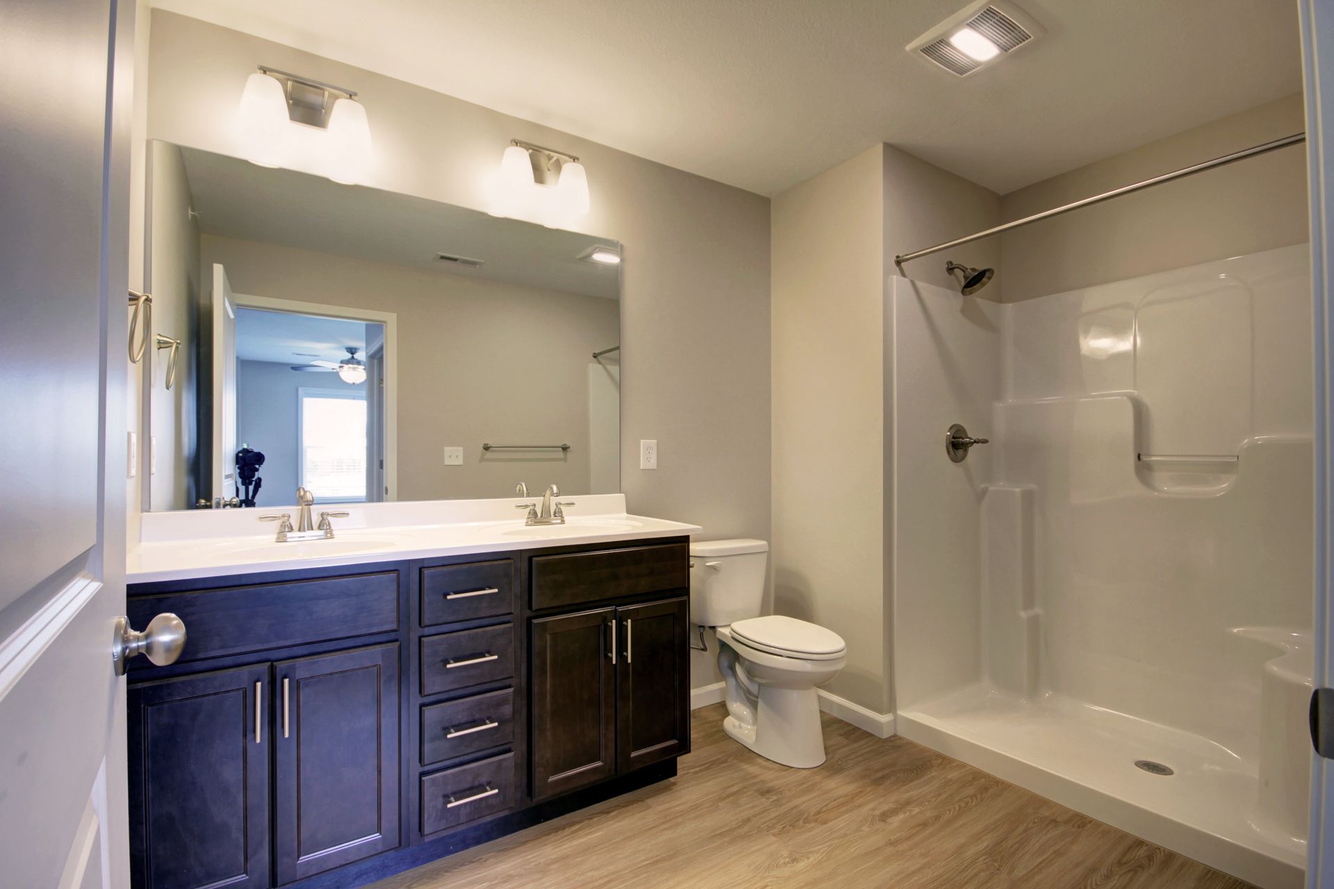 Modern bathroom with dark vanity, large mirror, toilet, and walk-in shower with glass door.