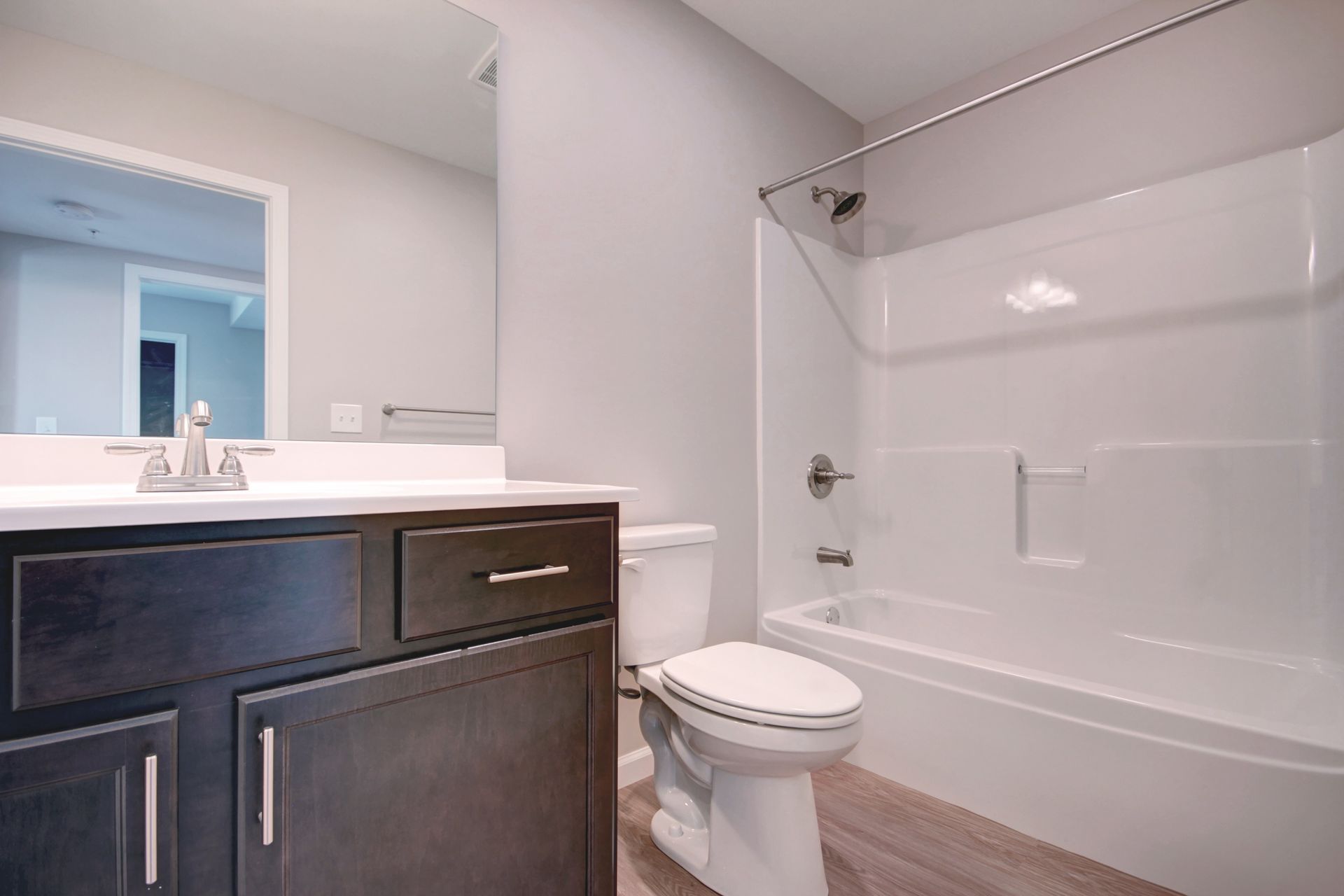 Modern bathroom with dark vanity, mirror, toilet, and white tub-shower combo